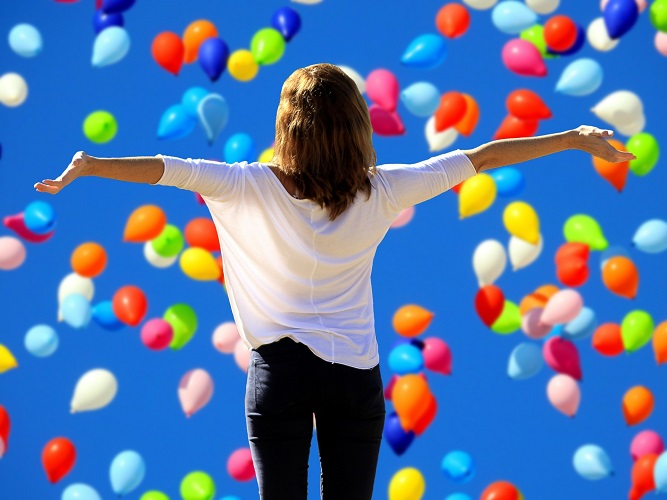 žena s otevřeno náručí a mnoho balonků stoupajících k obloze